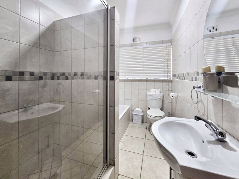 A well-maintained bathroom featuring a glass shower enclosure, a built-in bathtub, a pedestal washbasin, and neutral ceramic tiling throughout.
