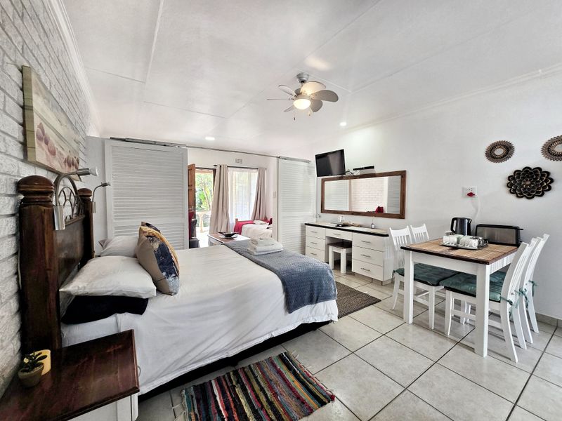 Spacious bedroom featuring tiled flooring, an exposed brick feature wall, a ceiling fan, and sliding doors leading to an outdoor area.