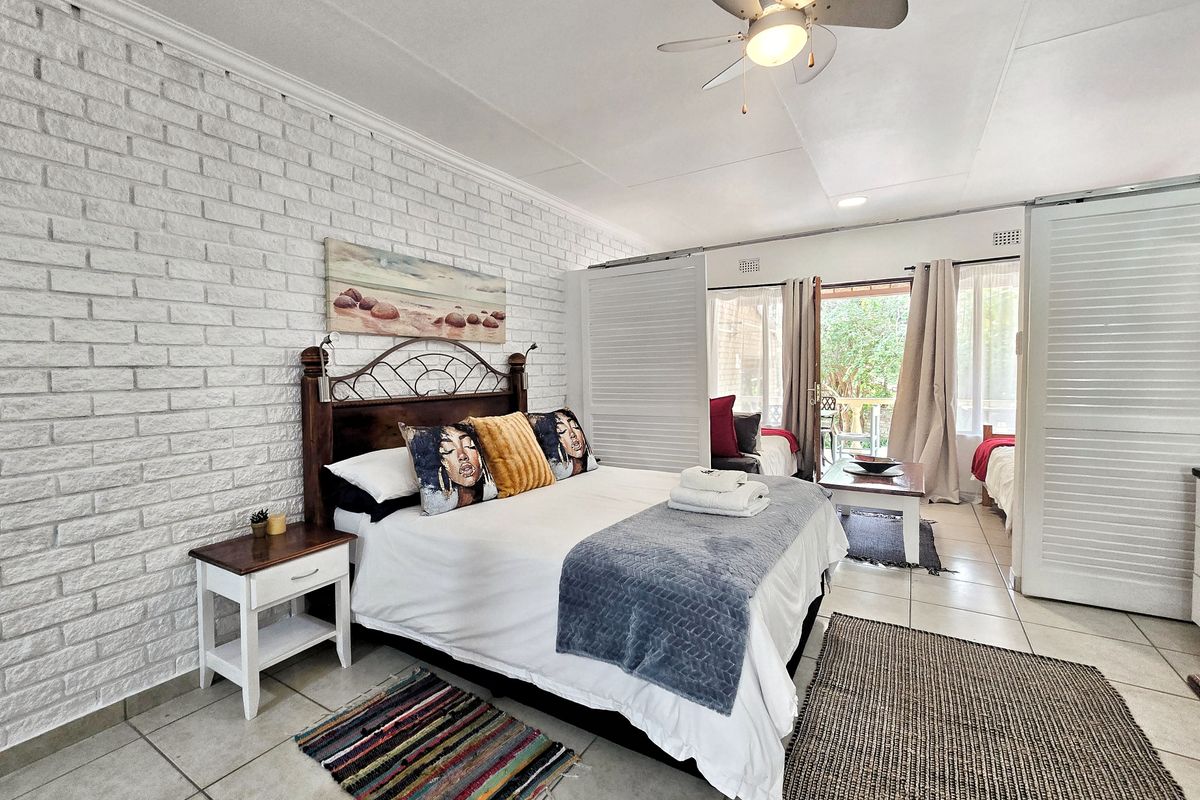 Spacious bedroom featuring a textured white brick feature wall, tiled flooring, ceiling fan, and sliding doors providing access to an outdoor patio area.