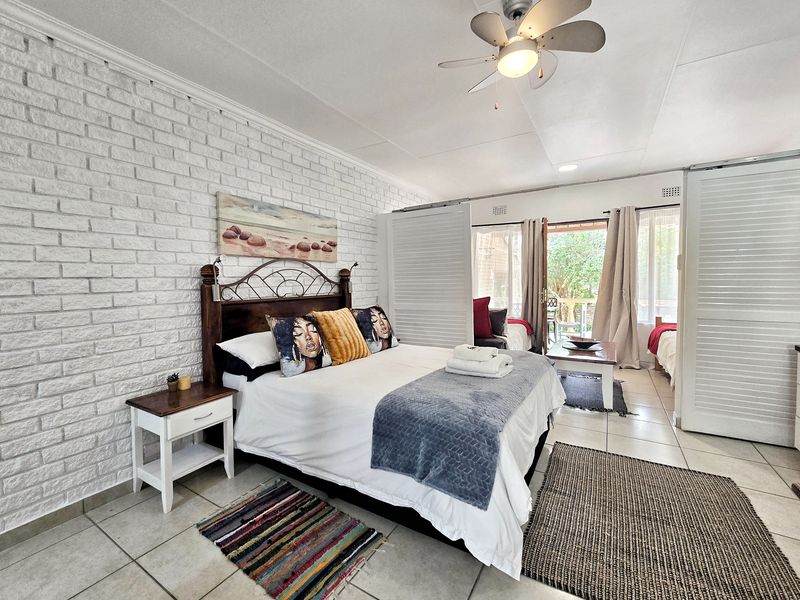 Spacious bedroom featuring a textured white brick feature wall, tiled flooring, ceiling fan, and sliding doors providing access to an outdoor patio area.