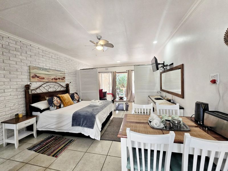 An open-plan studio apartment featuring tiled floors, an exposed brick feature wall, a ceiling fan, and sliding partitions leading to a private patio area.