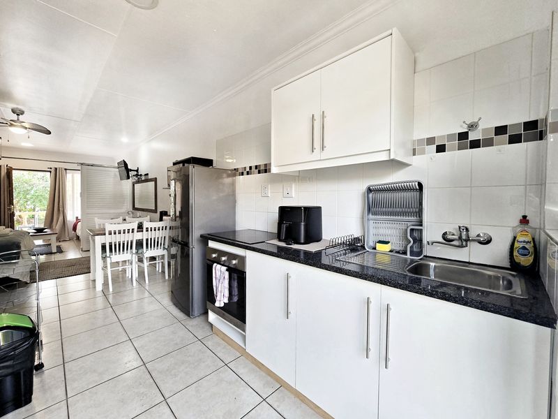 Open-plan kitchen featuring white cabinetry, granite countertops, and tiled flooring, seamlessly flowing into the adjacent dining and living area.