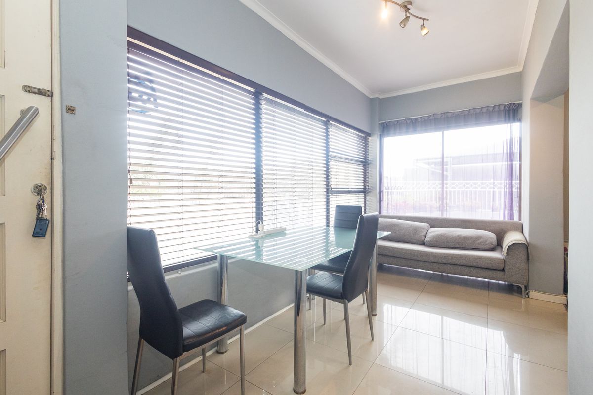 A bright living area featuring large windows with venetian blinds, tiled flooring, and a sliding door providing access to the exterior.