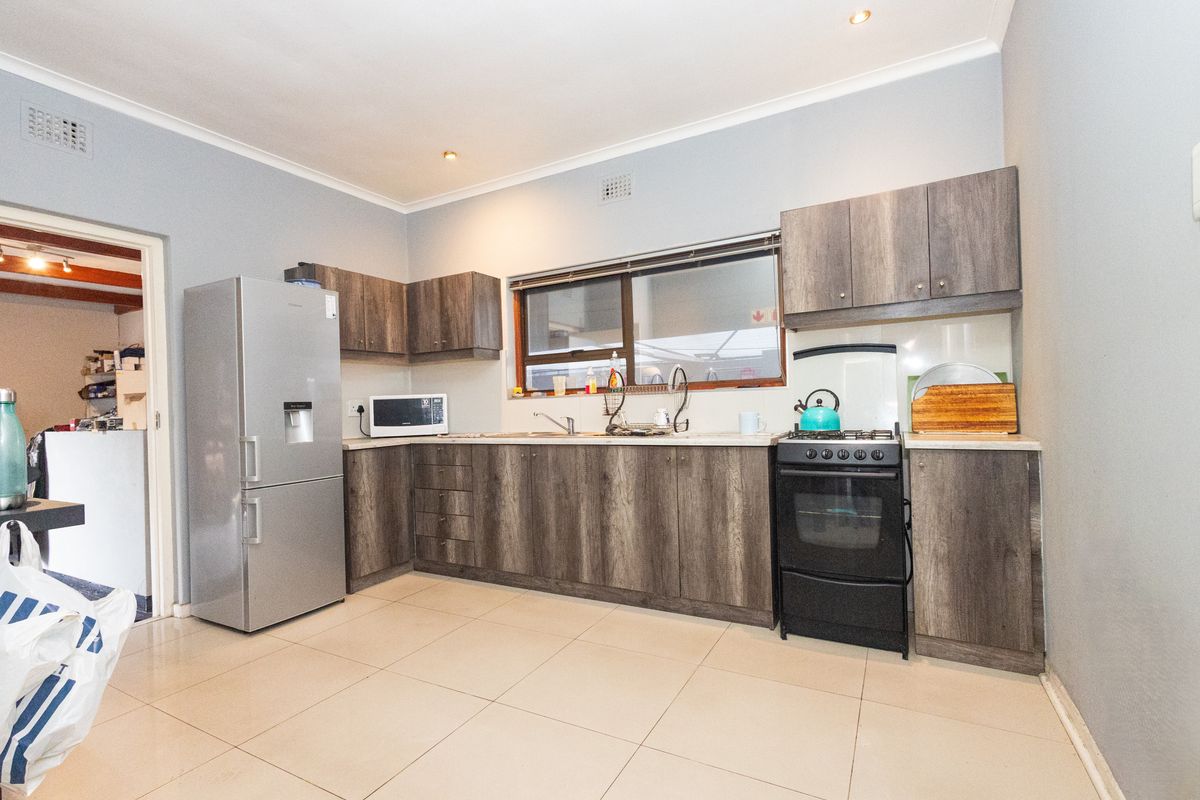 A functional kitchen featuring wood-look laminate cabinetry, stone-effect countertops, a freestanding oven, and neutral ceramic floor tiles.