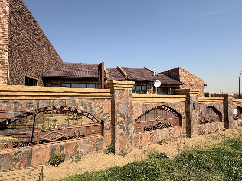Front exterior view of the property featuring a face brick facade, tiled roof, and a decorative stone-clad boundary wall with metal inserts.