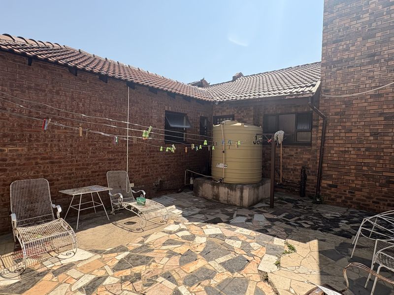 A rear courtyard area featuring face brick walls, a water storage tank, and paved flooring, offering potential for outdoor living space improvement.