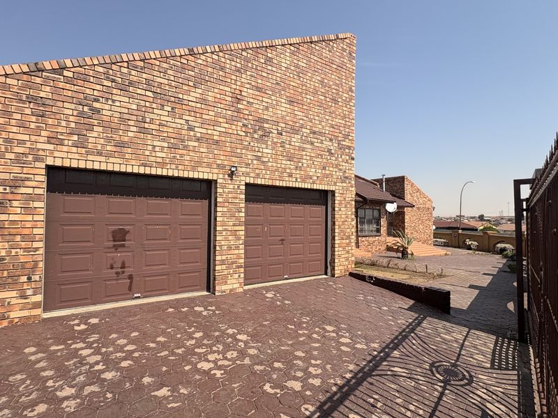 Front exterior view of the property featuring a double garage with brick facade and paved driveway access.