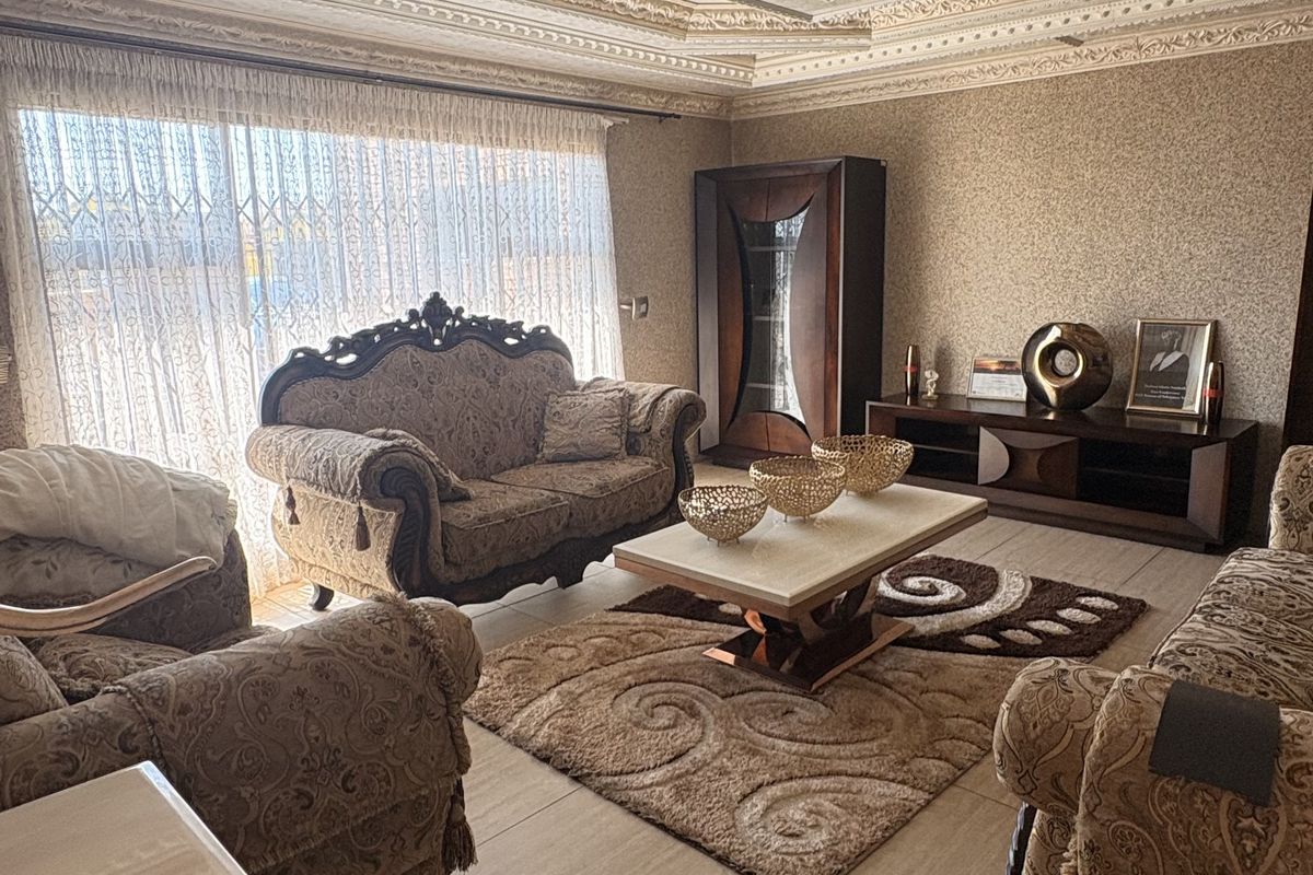 Spacious living room featuring an ornate coffered ceiling with a crystal chandelier, tiled flooring, and textured wallpaper, offering a formal and classic aesthetic.