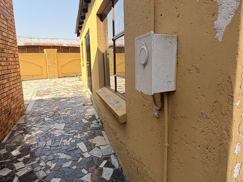 Side exterior walkway featuring crazy paving flooring and an external electrical distribution box mounted on a wall with peeling paint.