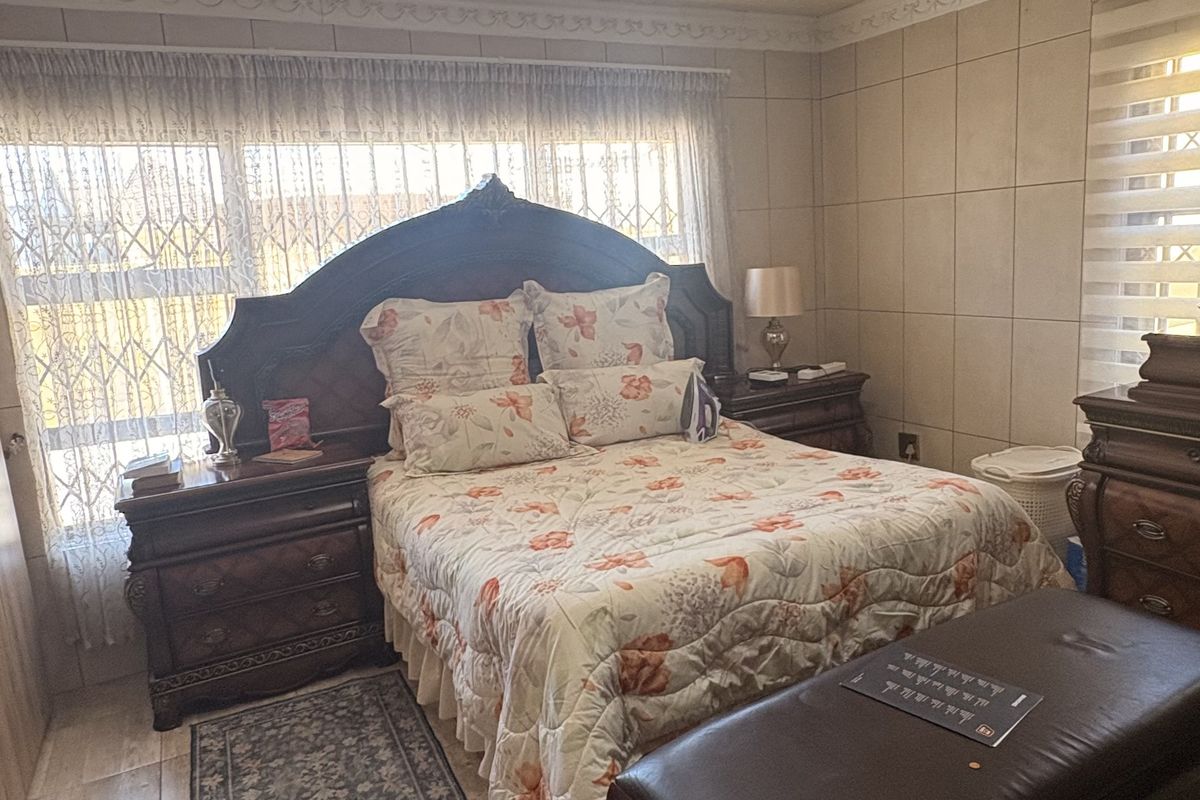 A bedroom featuring tiled flooring, textured ceiling finishes, and wall tiling, providing a functional space with security features on the windows.