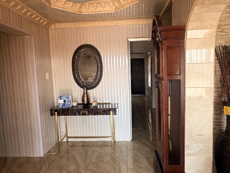 An elegant entrance hall featuring polished marble tile flooring, decorative wall paneling, and a detailed coffered ceiling with integrated lighting.