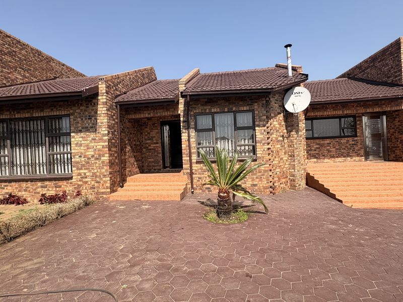 Front elevation of a face brick house featuring a paved driveway, tiled roof, and multiple entrance points with security gates.