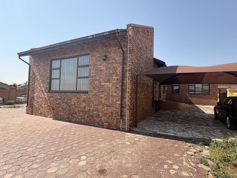 Front exterior view of a face brick house featuring a paved driveway and a shade cloth carport structure.