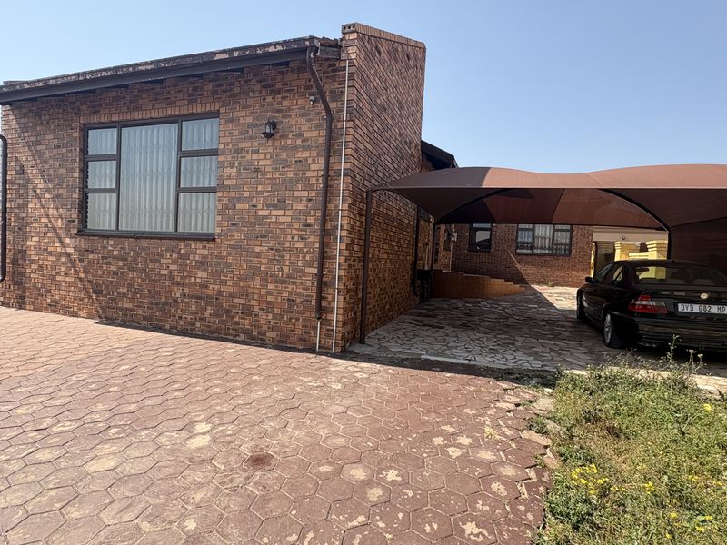 Front exterior view of a face brick house featuring a paved driveway and a covered carport area.