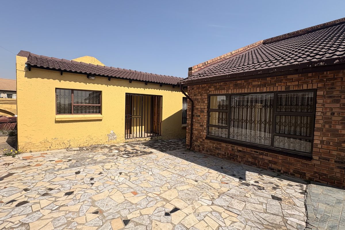Rear courtyard area featuring a mix of brick and plastered wall finishes, tiled roofing, and paved flooring with security bars on windows.