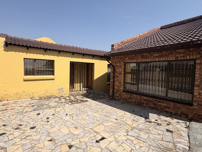 Rear courtyard area featuring a mix of brick and plastered wall finishes, tiled roofing, and paved flooring with security bars on windows.