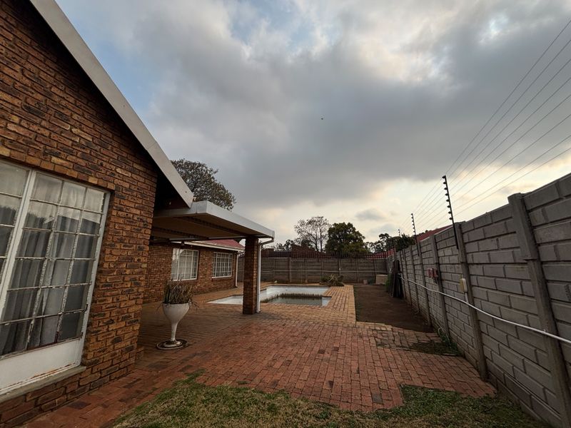 Rear exterior view featuring a brick-paved patio area, a swimming pool, and secure perimeter walling with electric fencing.