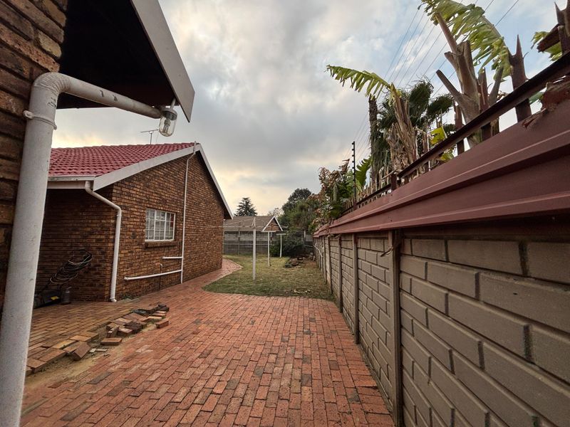 Rear exterior view featuring a brick-paved pathway, perimeter wall with electric fencing, and a brick house facade with a tiled roof.
