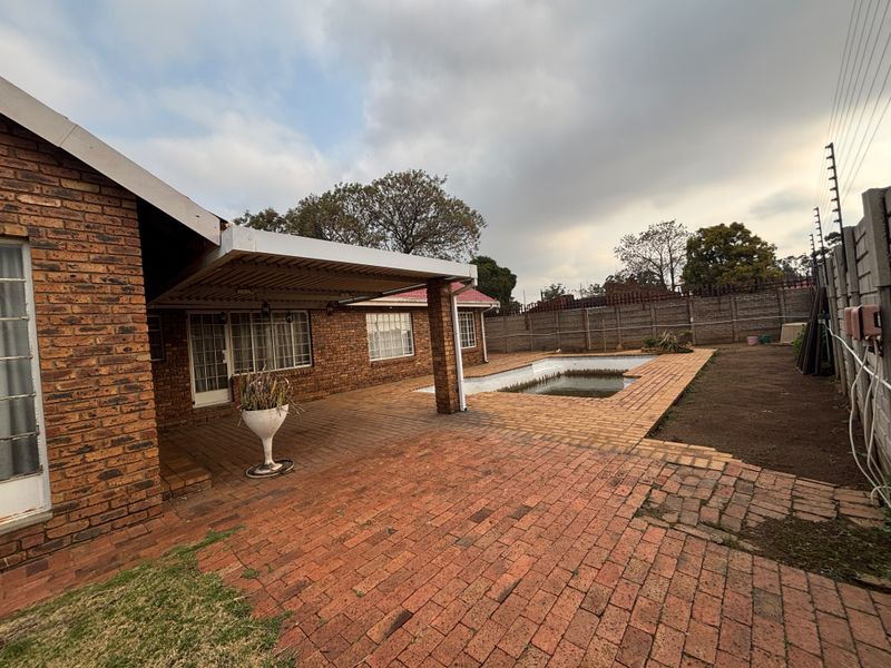 Rear exterior view featuring a brick-paved patio, a covered entertainment area, and an in-ground swimming pool enclosed by perimeter walling and electric fencing.