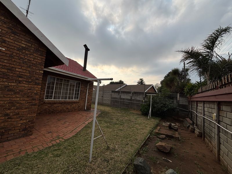 Rear garden area featuring a brick-faced house, paved patio section, perimeter walling, and a metal washing line structure.