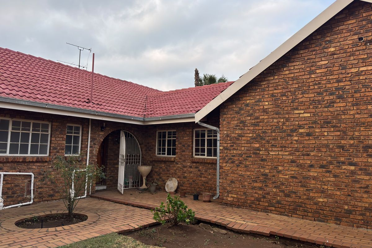Rear exterior view of the house featuring classic brick construction, a red tiled roof, and paved patio area.