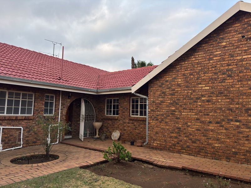 Rear exterior view of the house featuring classic brick construction, a red tiled roof, and paved patio area.