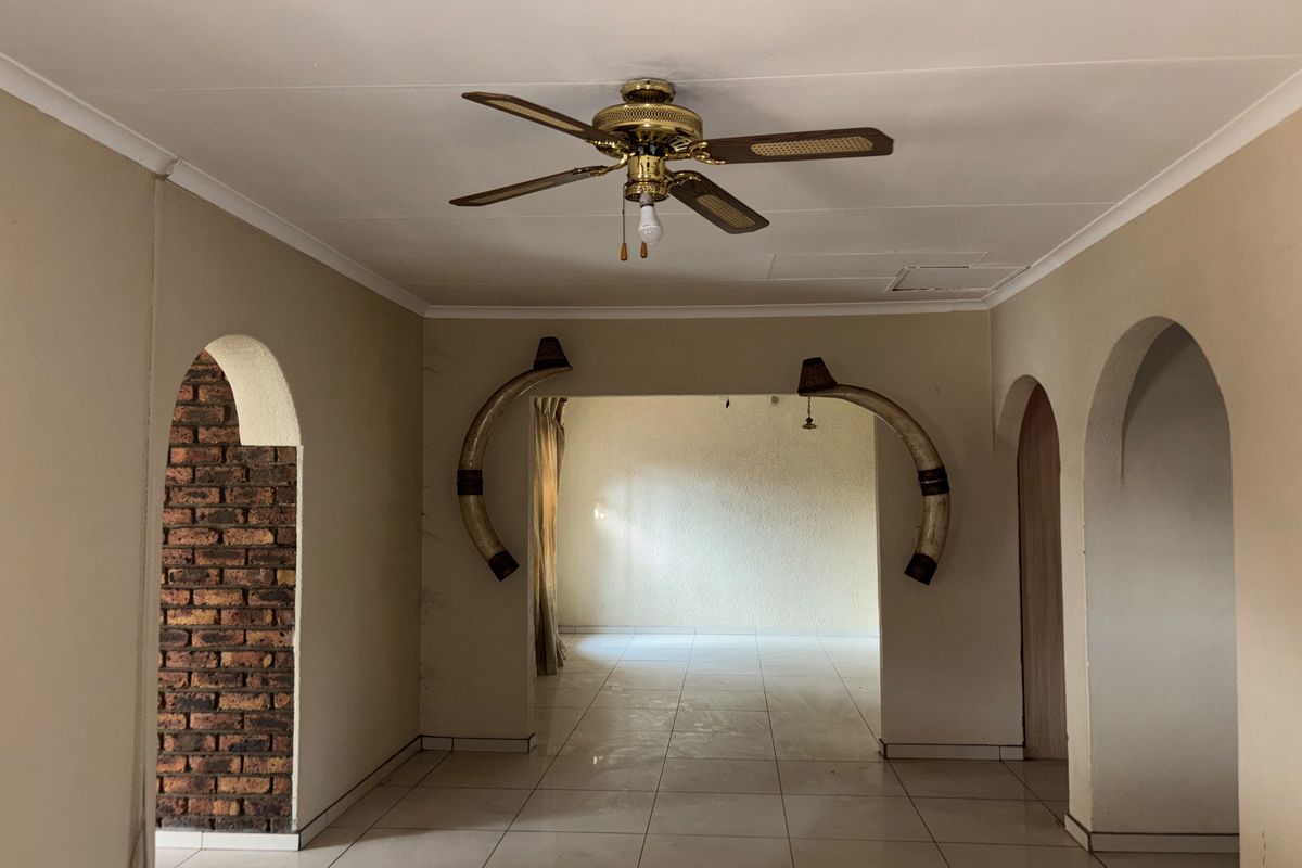 An open-plan living area featuring tiled flooring, a ceiling fan, and distinctive arched doorways with exposed brick detailing.