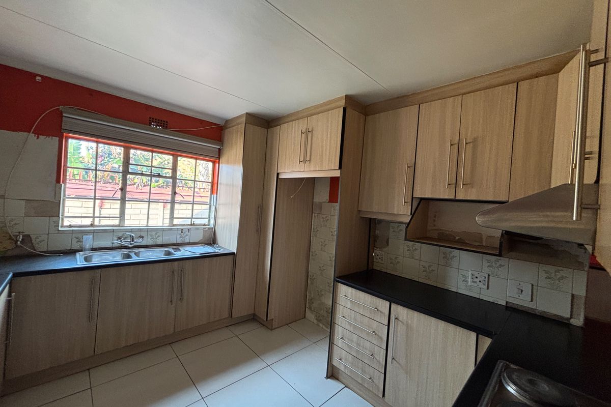 A functional kitchen featuring light wood-look cabinetry, double sink, and tiled flooring, currently requiring minor repairs and cosmetic updates to reach its full potential.