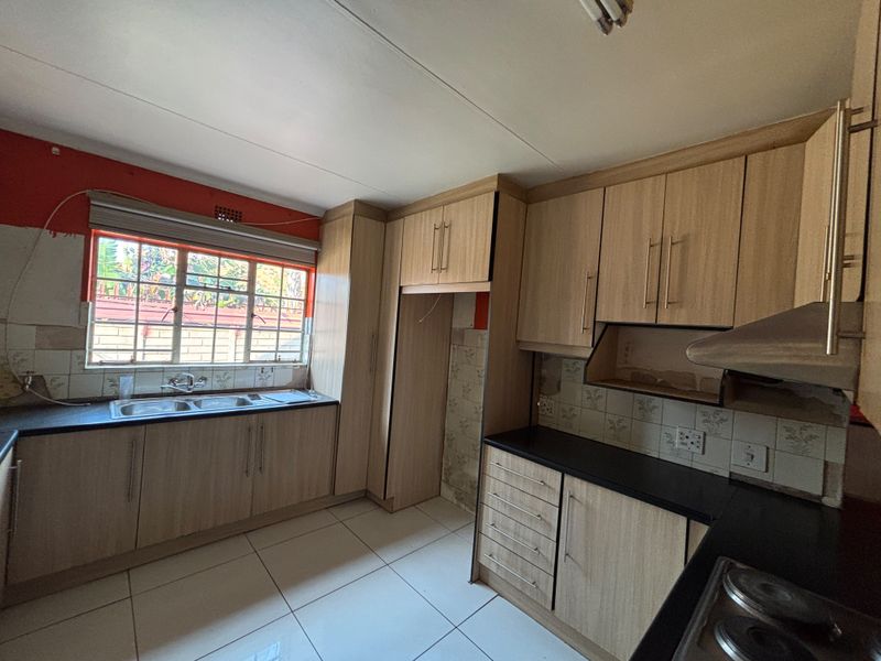 A functional kitchen featuring light wood-look cabinetry, double sink, and tiled flooring, currently requiring minor repairs and cosmetic updates to reach its full potential.