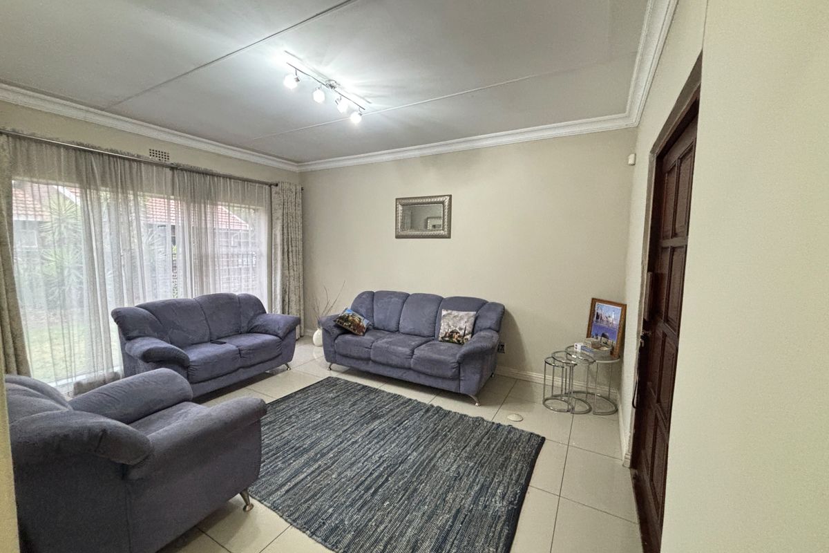 A spacious living room featuring neutral tiled flooring, decorative ceiling cornicing, and large sliding glass doors that provide ample natural light.