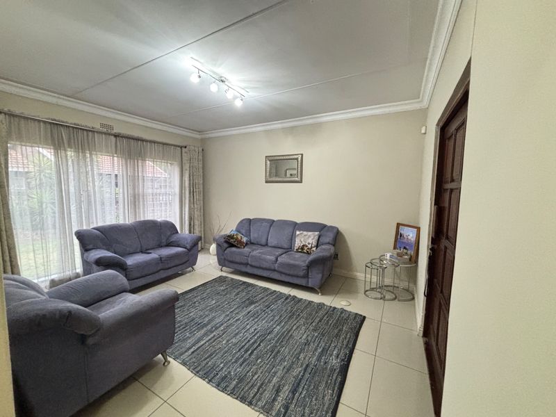 A spacious living room featuring neutral tiled flooring, decorative ceiling cornicing, and large sliding glass doors that provide ample natural light.