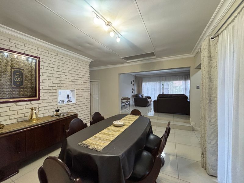 Open-plan dining and living area featuring a white brick feature wall, tiled flooring, and a pass-through window connecting to the kitchen.
