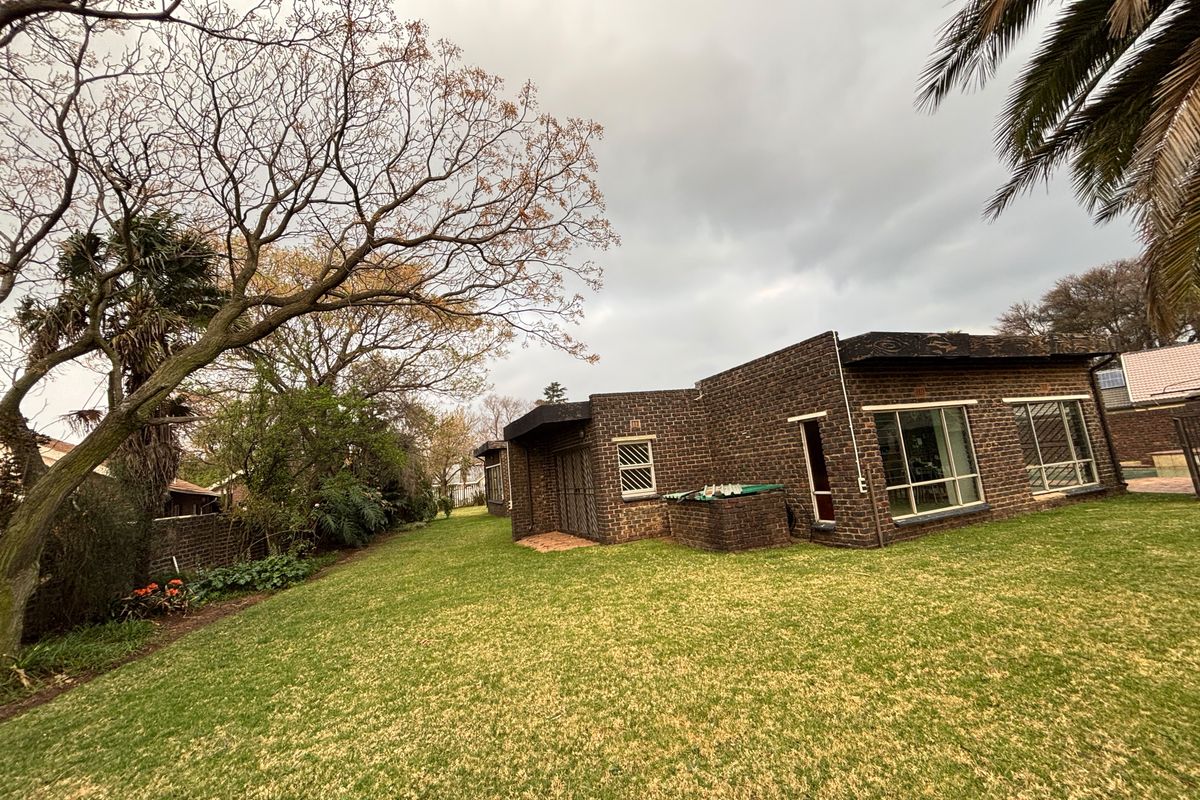 Rear view of the house featuring a face brick facade, large windows with security bars, and a spacious garden area with mature trees.