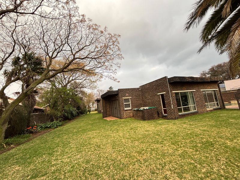 Rear view of the house featuring a face brick facade, large windows with security bars, and a spacious garden area with mature trees.