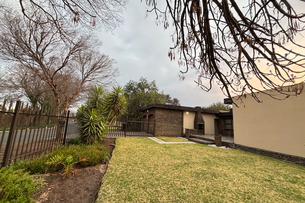 A rear garden view featuring a brick facade, a built-in braai on a paved patio, and established perimeter fencing.