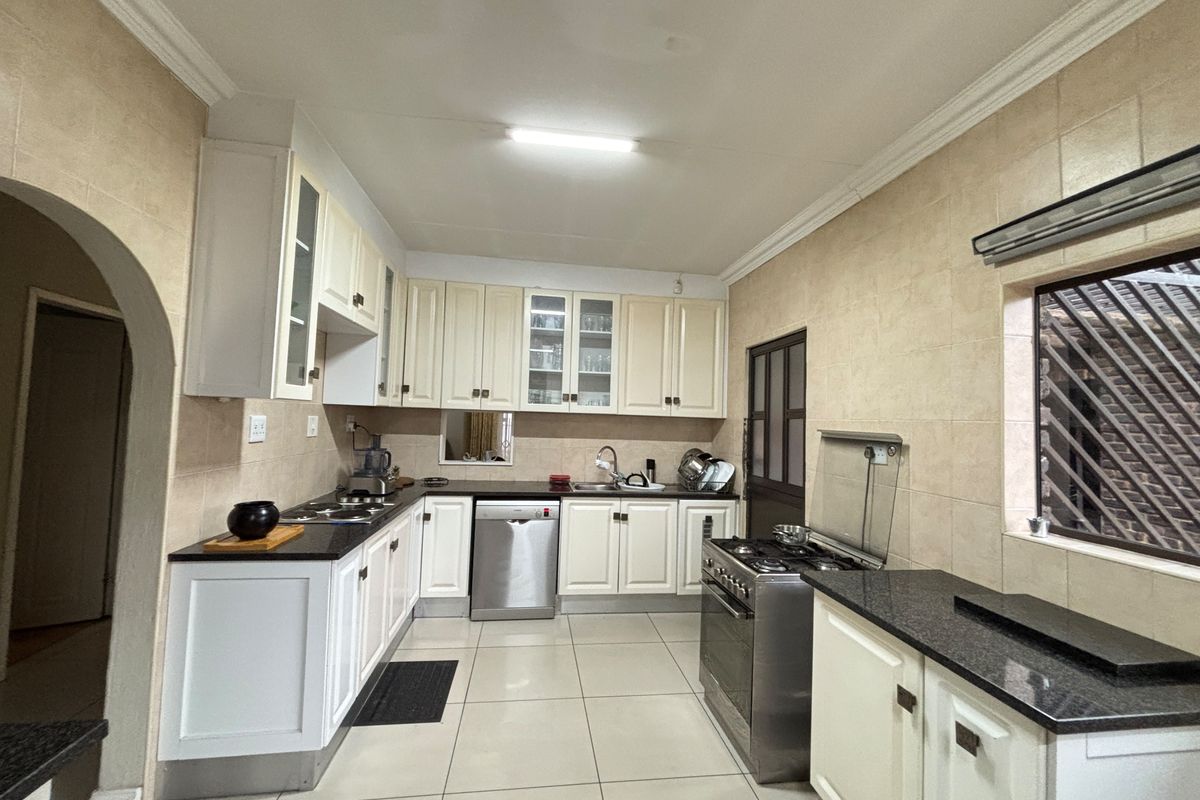 A functional kitchen featuring white cabinetry, granite countertops, stainless steel appliances, tiled flooring, and a classic archway entrance.