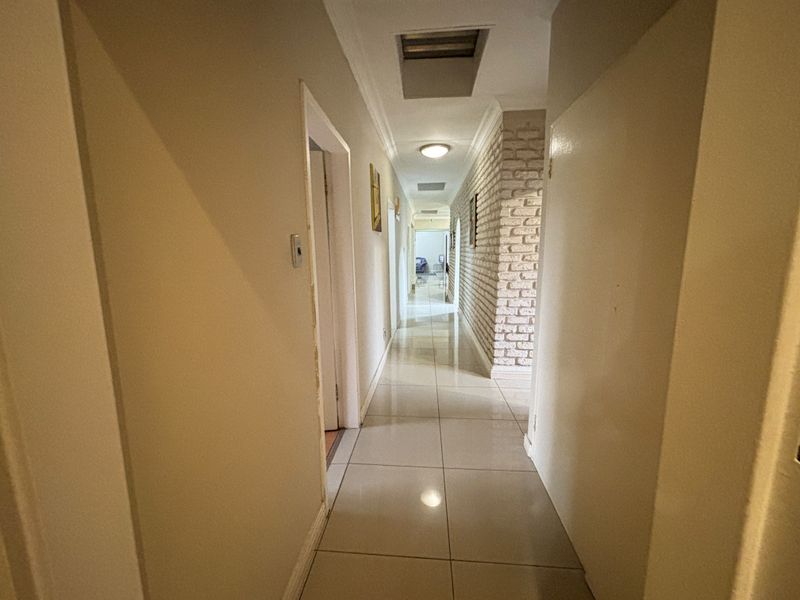 A long, bright hallway featuring polished floor tiles and a textured exposed brick feature wall, providing a clean and neutral transition between rooms.