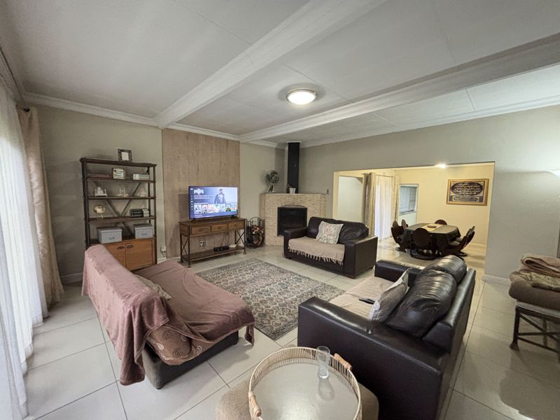 Spacious open-plan living and dining area featuring tiled flooring, a corner fireplace, and exposed ceiling beams, offering a functional layout for family living.