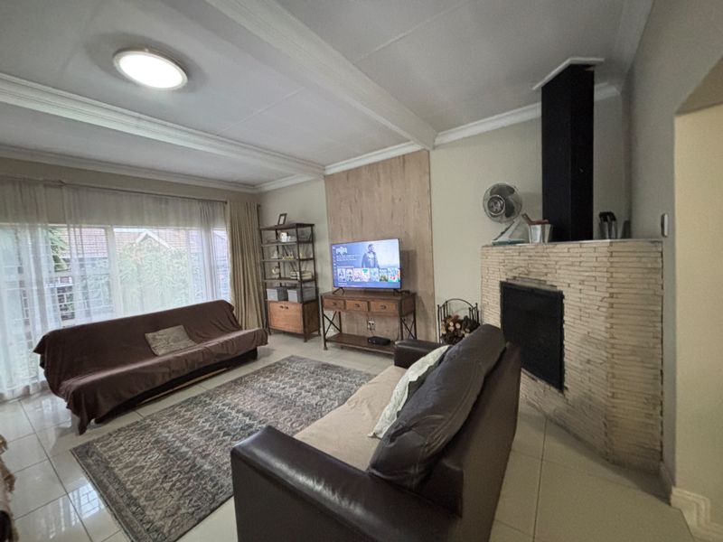 A comfortable living room featuring a prominent stone-clad fireplace, tiled flooring, and exposed ceiling beams, offering a cozy and functional space.