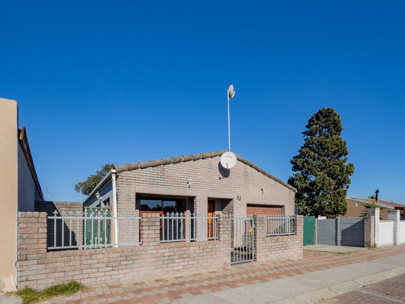 Front exterior view of a single-story brick house featuring a secure perimeter wall, metal fencing, and a paved entrance area.