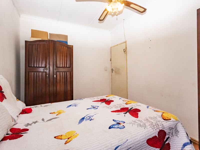 A compact bedroom featuring a ceiling fan and standard door access, requiring cosmetic updates to the wall finishes.