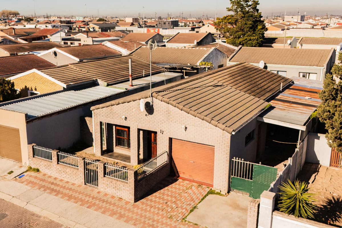 Aerial view of a single-story brick house featuring a tiled roof, attached garage, and paved driveway within a residential neighborhood.