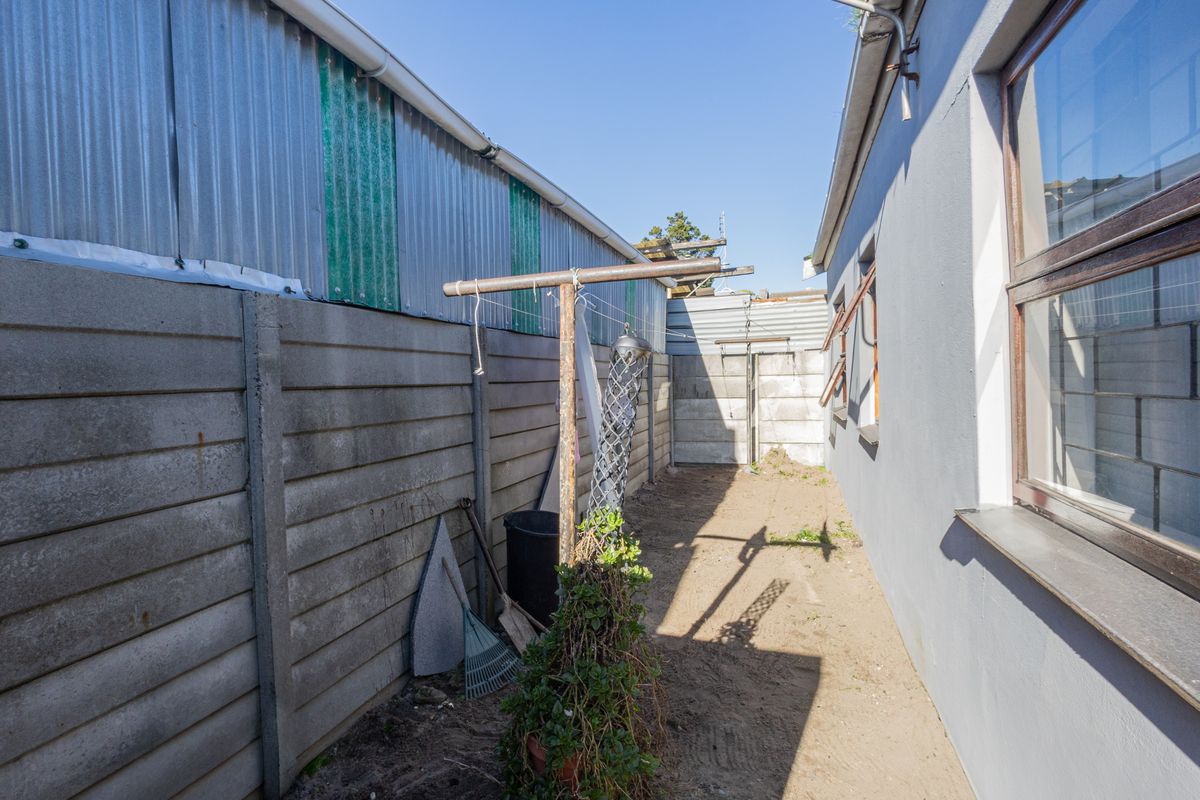 A narrow side or rear exterior passage featuring precast concrete boundary walls, corrugated metal siding, and aluminium window frames with security bars.