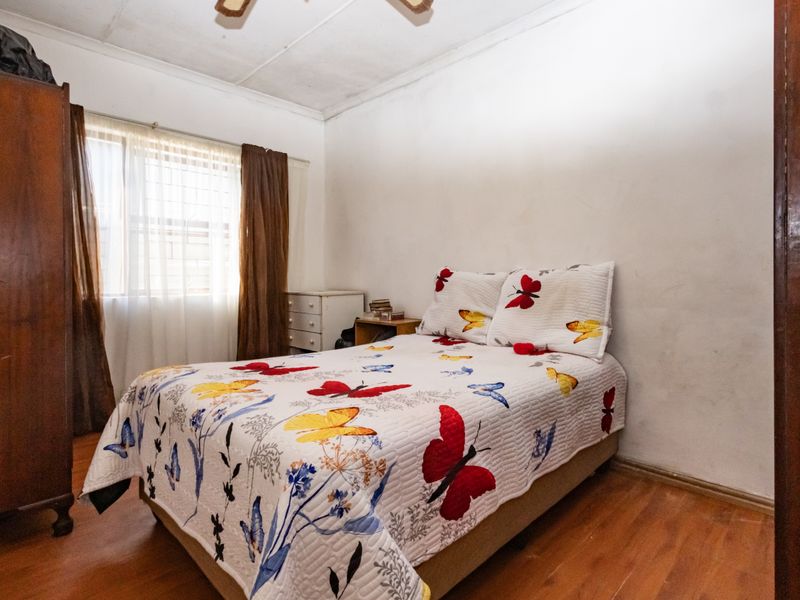 A bedroom featuring laminate flooring, a ceiling fan, and a window with security bars, showing signs of wear on the ceiling.