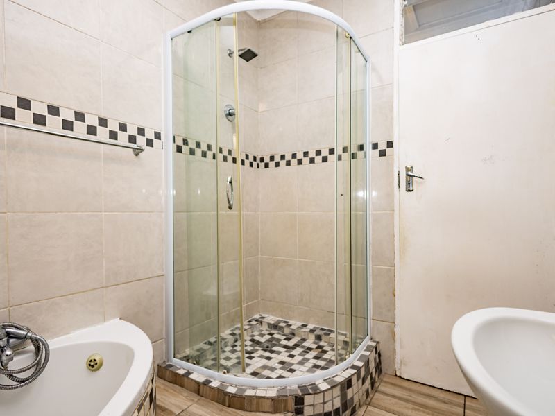 A functional bathroom featuring a corner shower enclosure, built-in bathtub, and tiled finishes throughout.