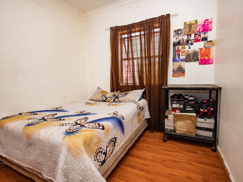 A compact bedroom featuring laminate flooring and a window fitted with security bars, offering a functional space ready for cosmetic updates.