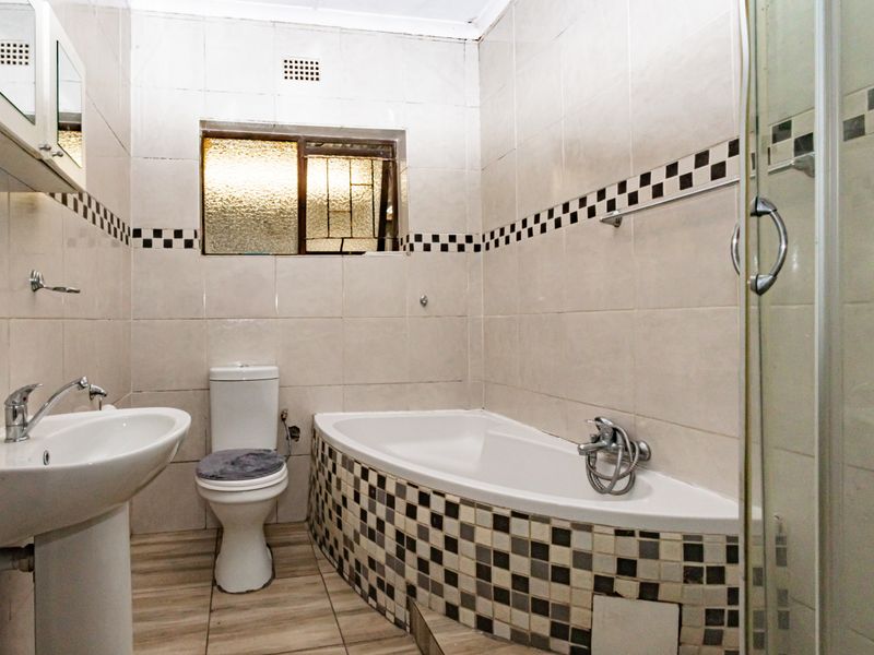 A functional bathroom featuring a pedestal basin, toilet, built-in bathtub with decorative tiling, and a separate shower enclosure.