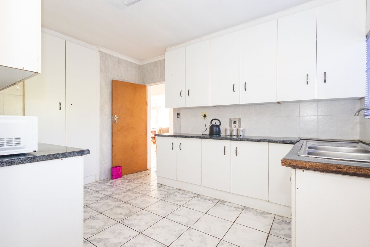 A functional kitchen featuring white built-in cabinetry, laminate countertops, a double stainless steel sink, and tiled flooring throughout.