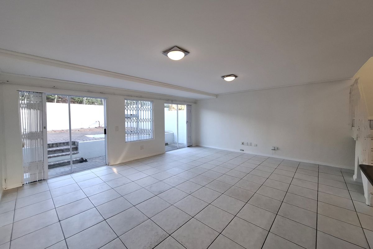 A spacious, empty living area featuring neutral tiled flooring, ample natural light from sliding glass doors, and direct access to an outdoor patio space.