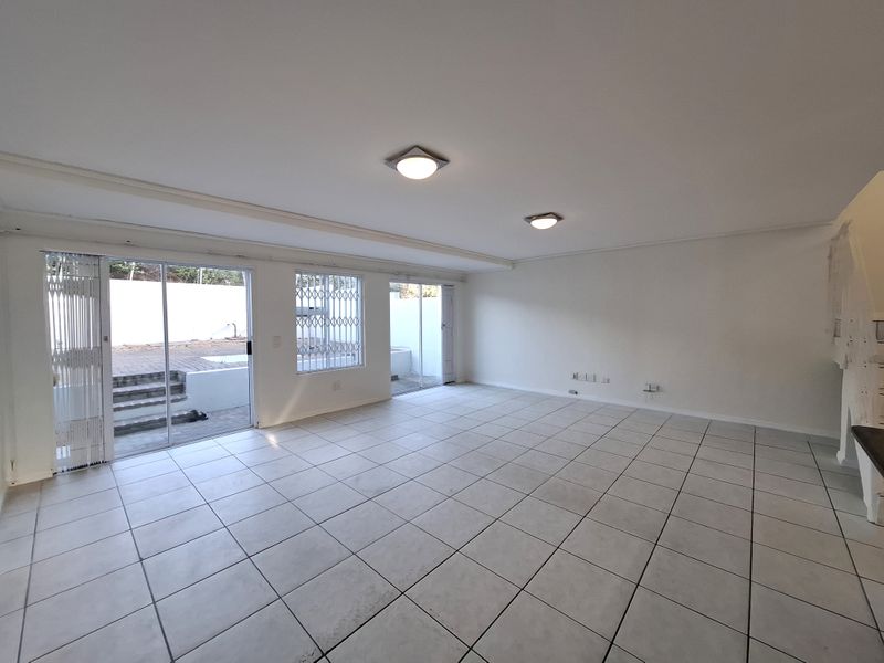A spacious, empty living area featuring neutral tiled flooring, ample natural light from sliding glass doors, and direct access to an outdoor patio space.